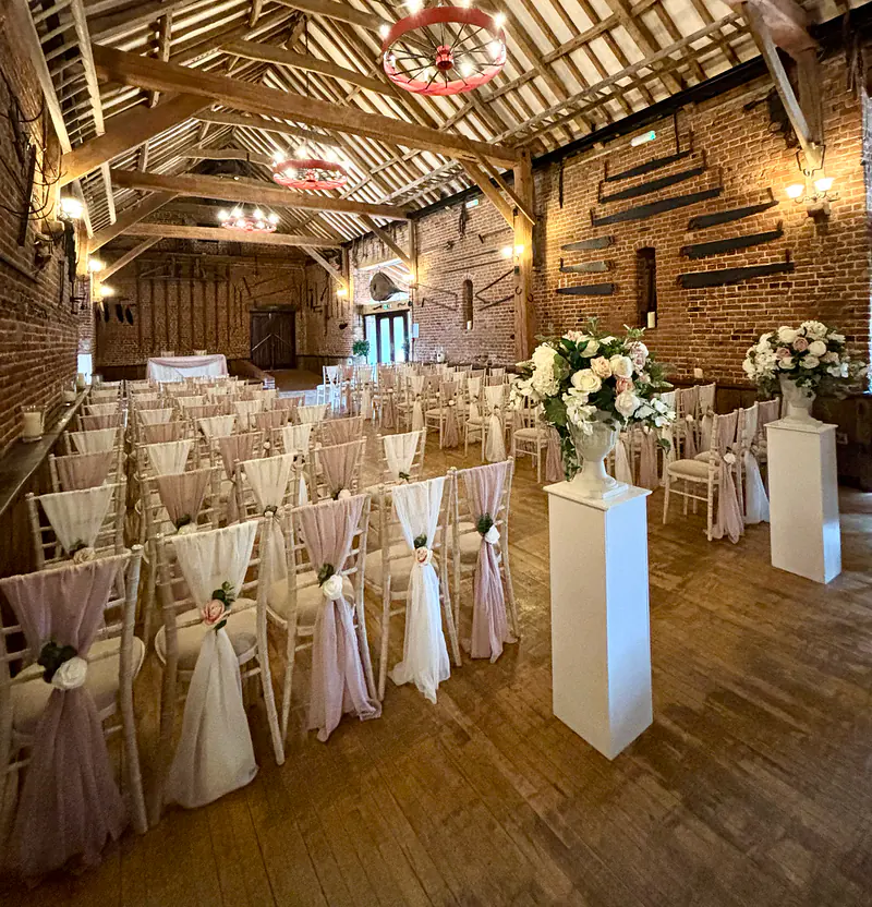 Large floral arrangements on tall white pedestals beside the aisle in a barn