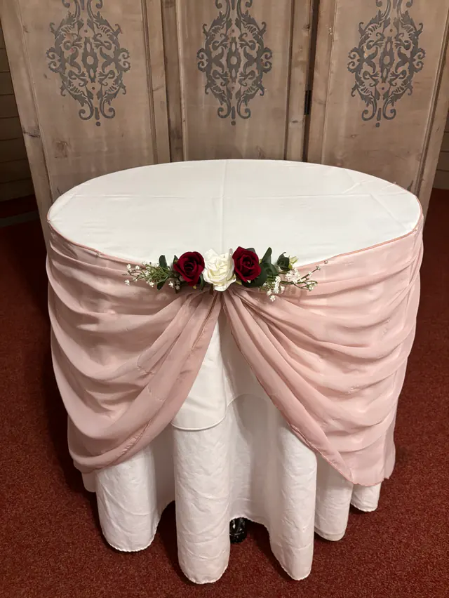 Round cake table with a pale pink chiffon swag finished with red and ivory roses