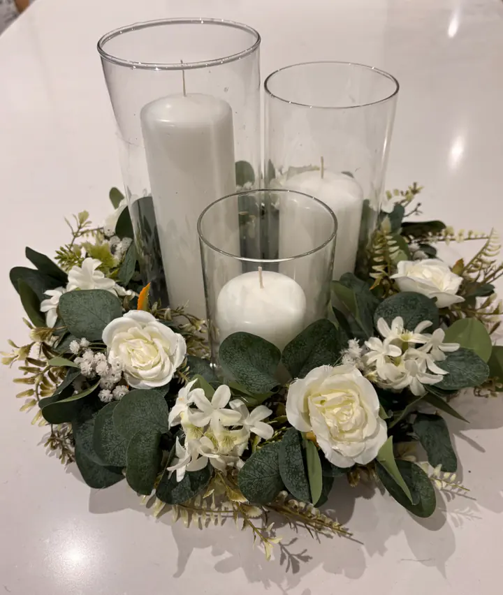 Eucalyptus wreath with ivory roses around three glass cylinder vases with candles