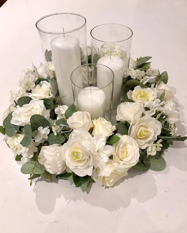 Ivory floral wreath around three glass cylinder vases with candles
