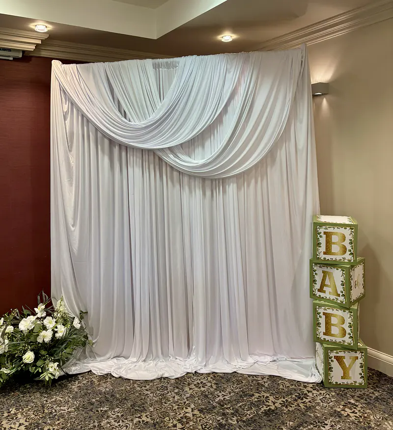 White draped backdrop with a swag across the top, set up for a baby shower