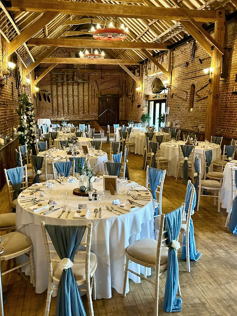 Dusky blue chiffon chair drapes with ivory roses at a wedding breakfast in the Victorian Barn at Hunters Hall