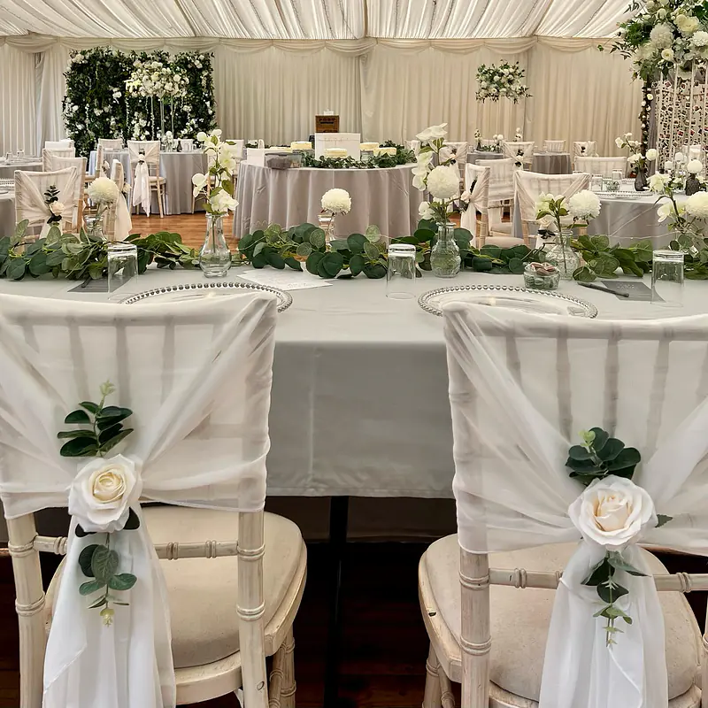 Ivory chiffon drapes styled as hoods, finished with ivory roses and a sprig of eucalyptus
