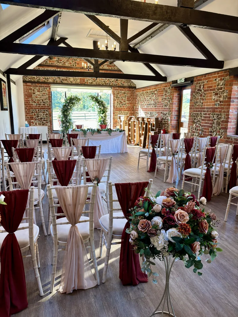Ceremony chairs with alternating rust and champagne chiffon drapes and a floral arrangement on a gold stand