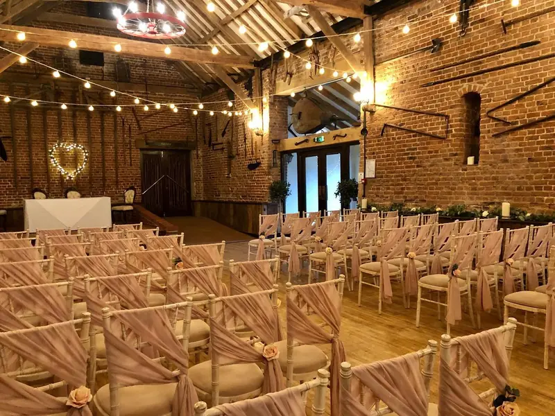 Barn ceremony room with pale pink chiffon chair drapes and festoon lights