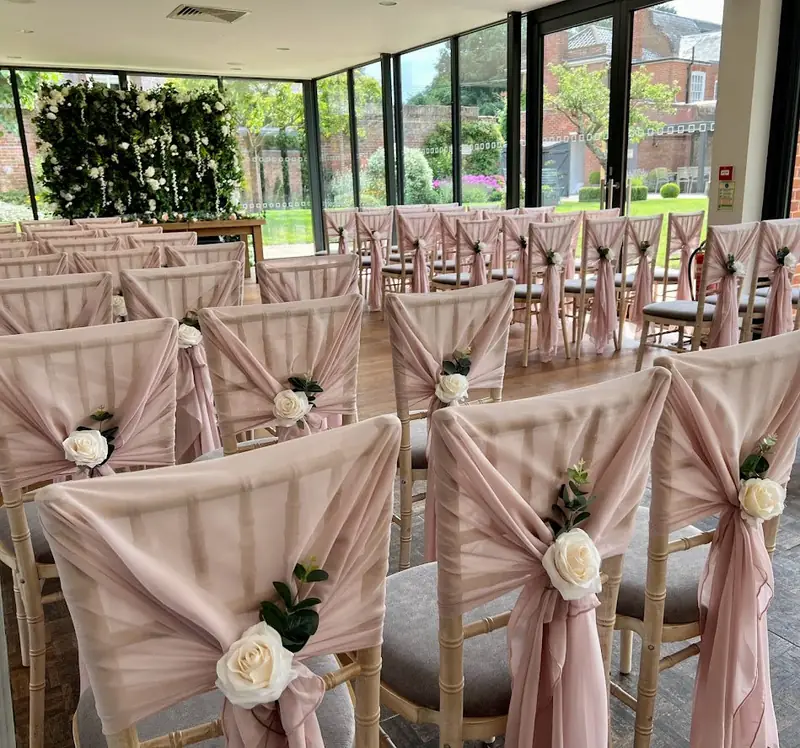 Ceremony chairs with pale pink chiffon drapes, ivory roses and sprigs of eucalyptus