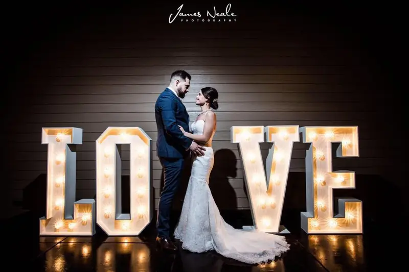 Bride and groom standing between white light-up LOVE letters