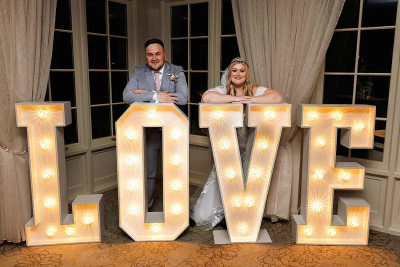 Bride and groom leaning on white light-up LOVE letters