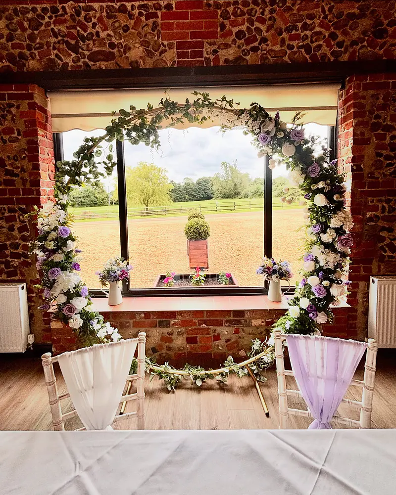 Moon gate dressed with greenery and ivory and lilac flowers in front of a window in the Park Room at Hunters Hall