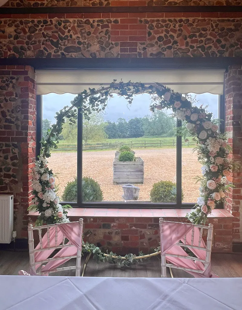 Moon gate with pink flowers in front of a window, behind two chairs with pink drapes