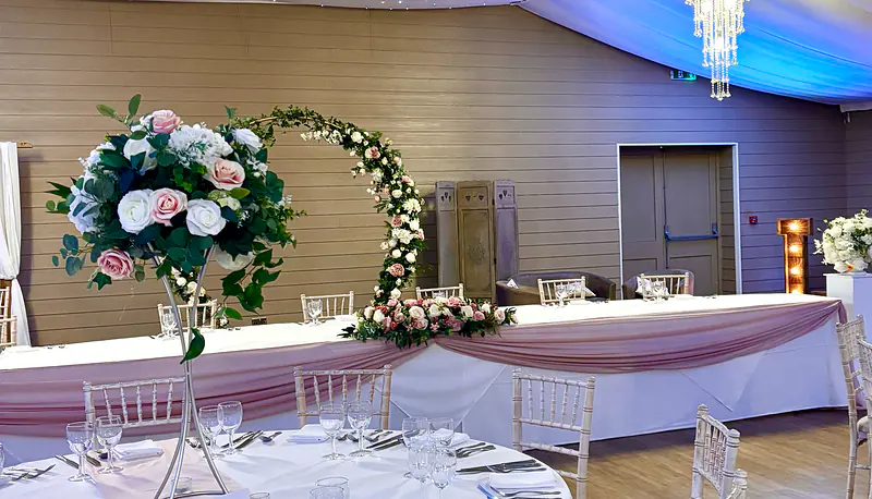Moon gate behind a top table with a pale pink swag and a floral arrangement