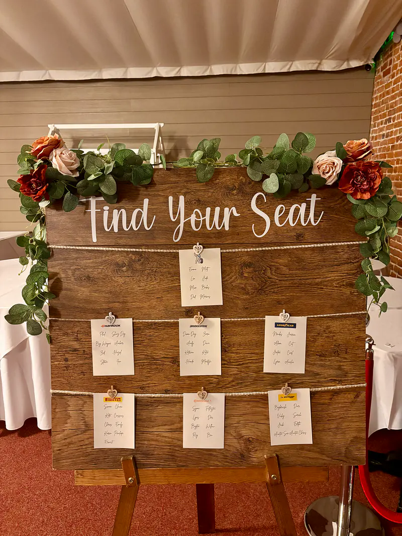 Rustic wooden table plan on an easel, with seating cards pegged to twine and a eucalyptus garland