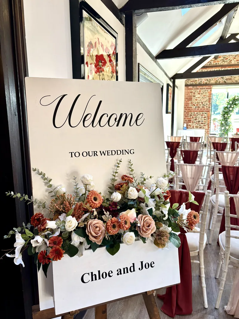 White welcome sign dressed with rust, peach and ivory flowers