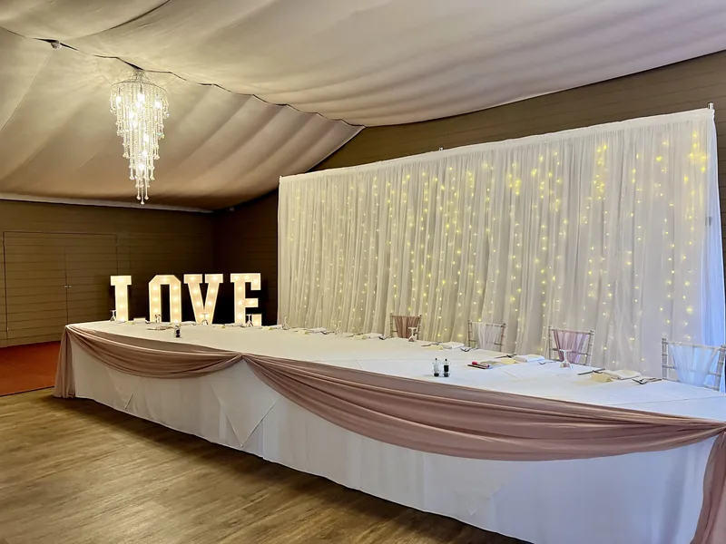Starlit backdrop with soft-glow lights behind a long top table with a pale pink swag, beside light-up LOVE letters