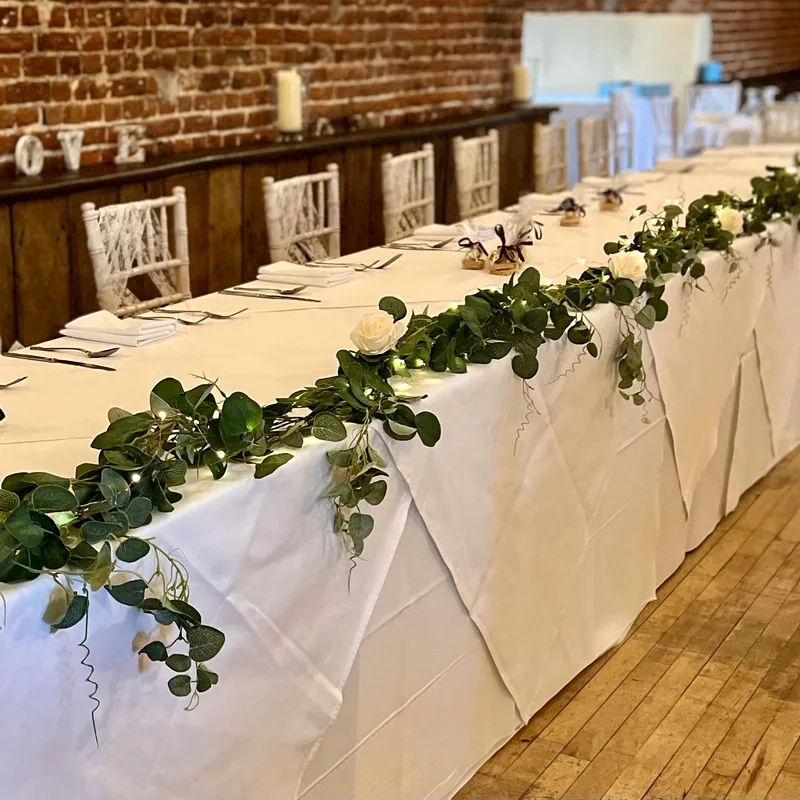 Long top table in a barn with a greenery garland and ivory roses