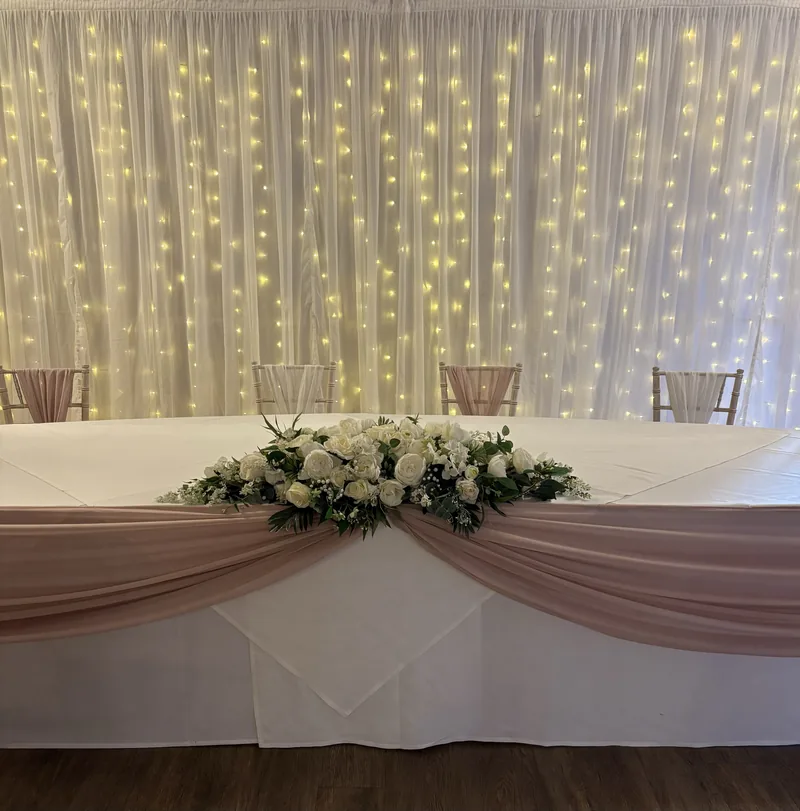 Top table with an ivory long and low floral arrangement and a pale pink swag, in front of a starlit backdrop