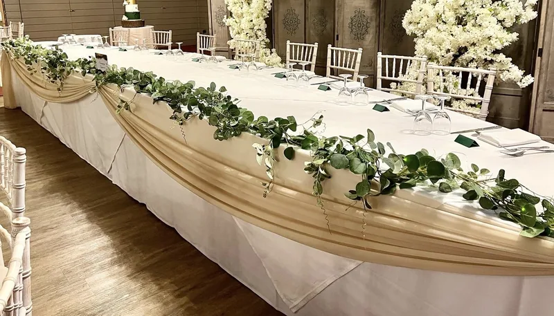 Long top table with a champagne chiffon swag and a greenery garland