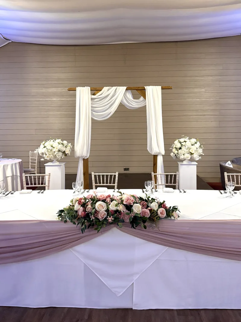Rustic wooden arch with ivory chiffon drapes behind a top table with a pale pink swag
